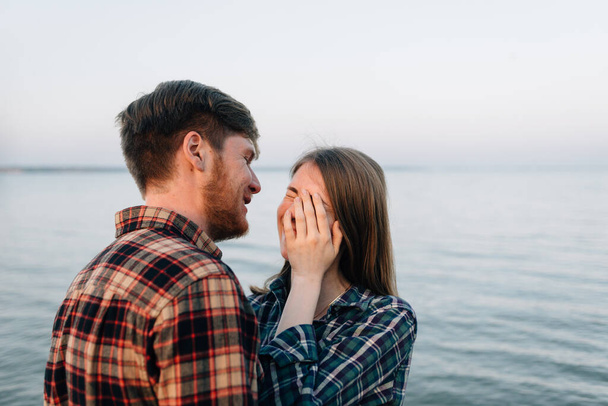 portré Y-generációs pár csókolózás a strandon a tenger mellett. Egy szakállas férfi és egy barna lány ölelkezik a víz mellett. szerelmesek diákok.Pihenjen a tenger vagy az óceán. szezon Ősz. - Fotó, kép