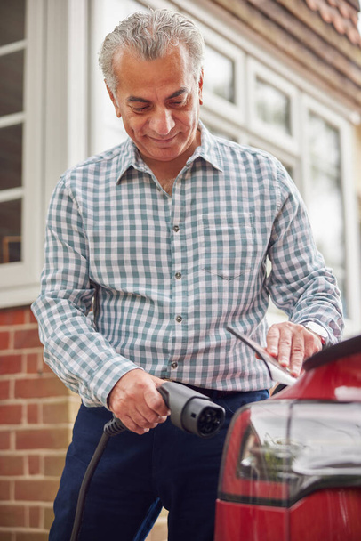 Mature Man Attaching Charging Cable To Environmentally Friendly Zero Emission Electric Car At Home - Fotoğraf, Görsel