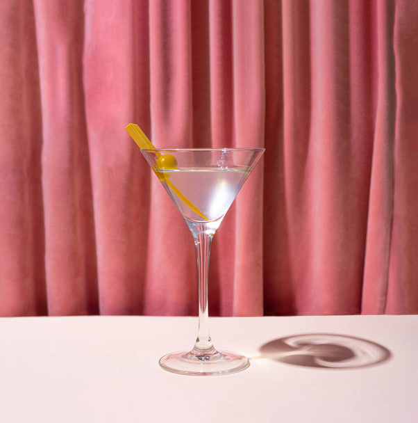Ένα ποτήρι κοκτέιλ, μαρτίνι μπροστά από την ροζ βελούδινη κουρτίνα αναγέννησης. Αναδρομική ατμόσφαιρα θεάτρου. - Φωτογραφία, εικόνα
