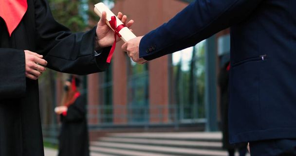 Cropped view of the two graduated students shaking hands to each other while standing near the university after the graduation. People holding their diplomas - Zdjęcie, obraz