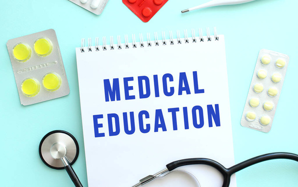 テキスト医学教育は青い背景に聴診器や丸薬の隣にあるノートに青で書かれています。医学的概念 - 写真・画像