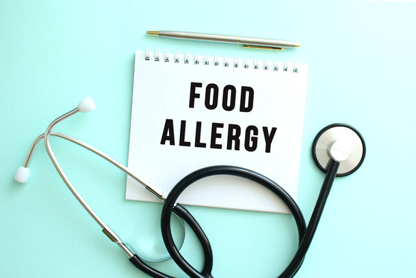 White notepad with the words FOOD ALLERGY and a stethoscope on a blue background. Medical concept - Photo, Image
