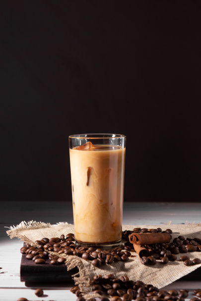 Un vaso de café frío y crema. Granos de café, fondo oscuro. Vista lateral, foto vertical. - Foto, imagen