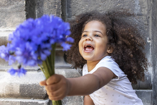 Εξωτερική πορτρέτο ενός σγουρού Αφροαμερικανού κοριτσιού με ένα μπουκέτο μπλε λουλούδια. - Φωτογραφία, εικόνα
