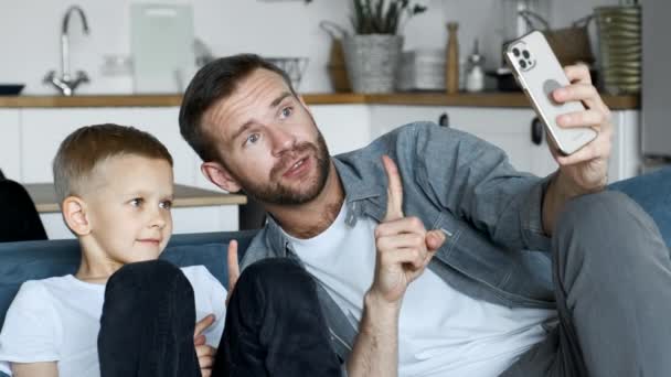 El padre joven pasa tiempo con su hijo divirtiéndose usando el teléfono inteligente en casa - Metraje, vídeo