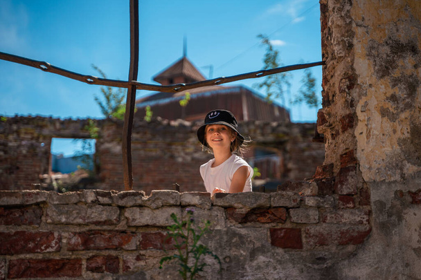 Egy kislány egy lerombolt épület fém kerítése mögött, a gyermekvédelem fogalma. - Fotó, kép