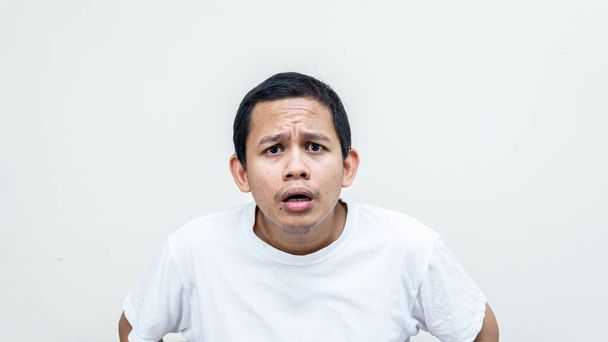 Ένα πορτραίτο ενός Ασιάτη Μαλαισιανού με λευκό μπλουζάκι που θύμωνε και θύμωνε, κατσουφιάζοντας το κεφάλι του στην κάμερα σε απομονωμένα λευκά υπόβαθρα. Γεμάτο θυμό.. - Φωτογραφία, εικόνα