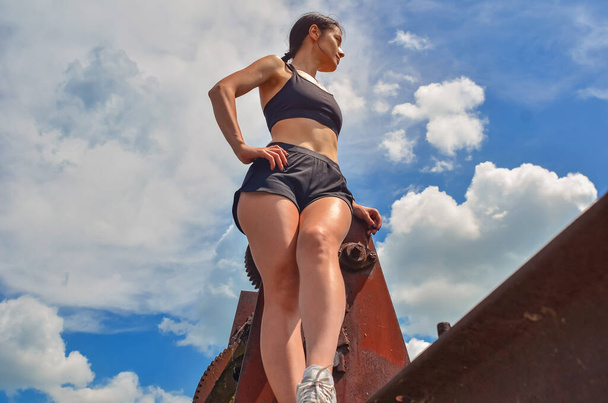Chica atlética en pantalones cortos deportivos negros y soportes superiores en el fondo de la vista del cielo desde abajo - Foto, Imagen