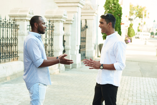 Gelukkige twee multiraciale mannelijke beste vrienden praten terwijl ze op straat staan, Afrikaanse man praten met Afghaanse vriend op outdoor bijeenkomst. Lachende multi-etnische jongeren, multiculturele vriendschap reünie - Foto, afbeelding