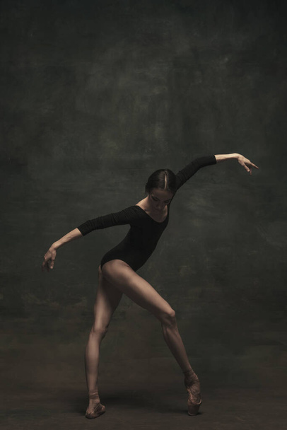 Jonge en sierlijke balletdanser geïsoleerd op donkere achtergrond. Kunst, beweging, actie, flexibiliteit, inspiratie. - Foto, afbeelding