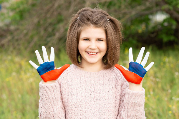Dziecko dziewczyna pokazać ręce malowane w Rosji flagi kolory spaceru na świeżym powietrzu. Dzień rosyjskiej flagi. Obywatelstwo patriotów. 12 czerwca. 22 sierpnia wakacje. 4 listopada - Zdjęcie, obraz