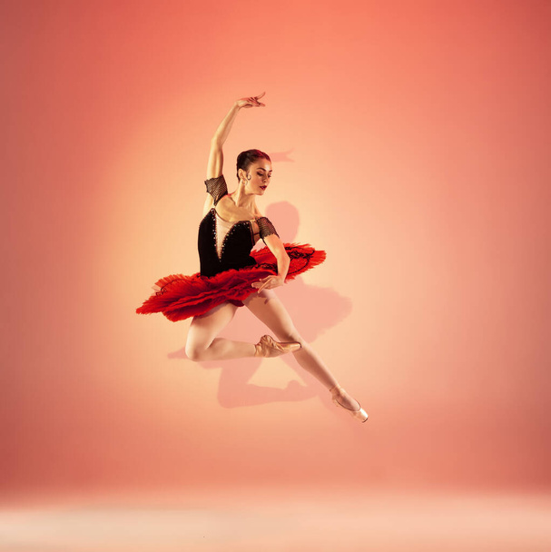 Young and incredibly beautiful ballerina is posing and dancing at red studio full of light. - Фото, изображение