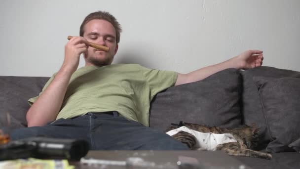 未使用の葉巻を嗅ぎ、ソファに座っている若い男,薬物とアルコールの害の概念,屈託のない生活 - 映像、動画
