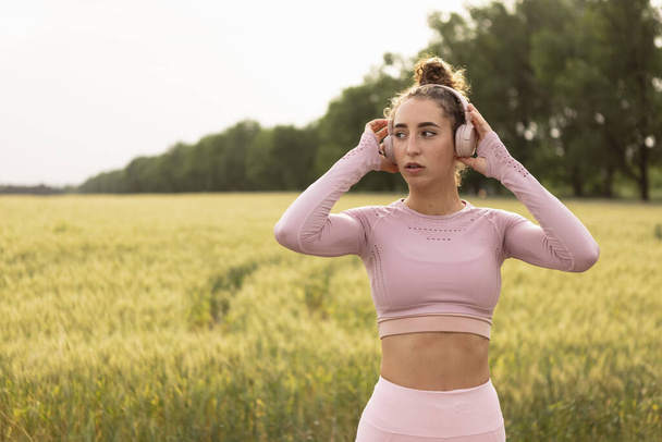 Young female runner, athlete is jogging at road in summer sunshine. Beautiful caucasian woman training, listening to music. Concept of sport, healthy lifestyle, movement, activity. - Photo, image
