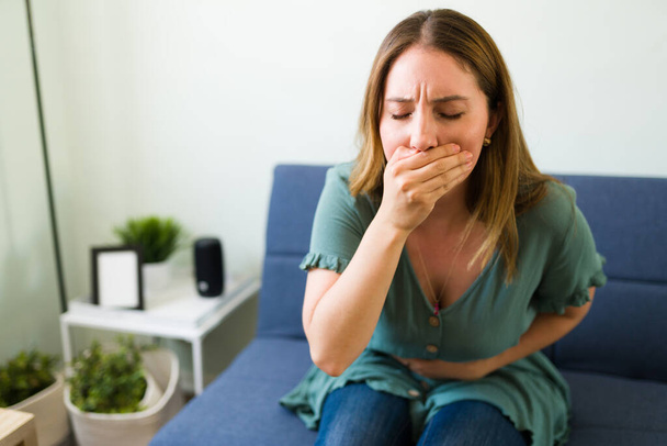 Attractive woman in her 20s about to vomit in the living room because of her stomach infection after eating bad food - Photo, Image