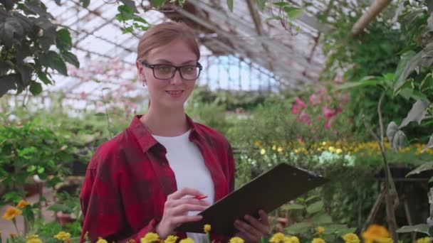 Portrét mladého pracovníka ve skleníku, ve kterém rostou květiny a rostliny, dívčí inspektor - Záběry, video