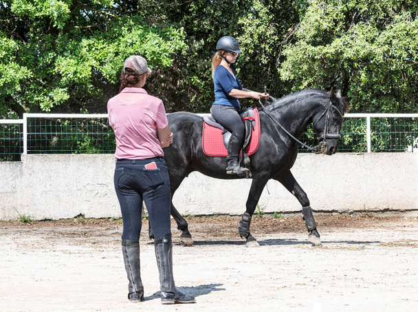  ιππασία κορίτσι και δάσκαλος εκπαιδεύουν μαύρο άλογο της - Φωτογραφία, εικόνα