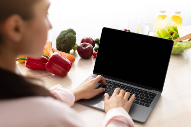 Boş ekranlı dizüstü bilgisayar kullanan bir kadın masada oturuyor - Fotoğraf, Görsel