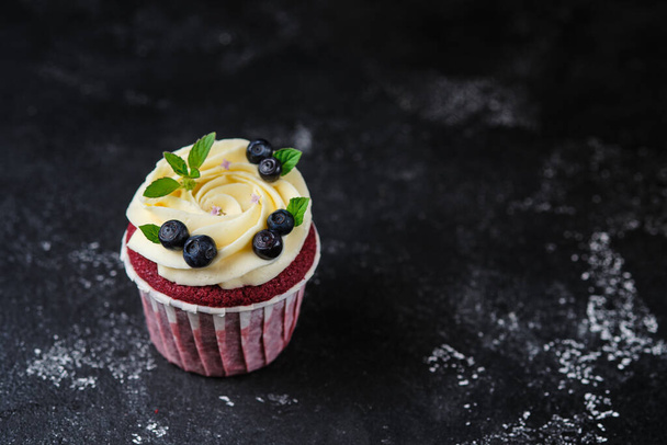 Red velvet cupcakes with cream cheese cream. Dessert garnished with fresh blueberries and mint. - Foto, afbeelding