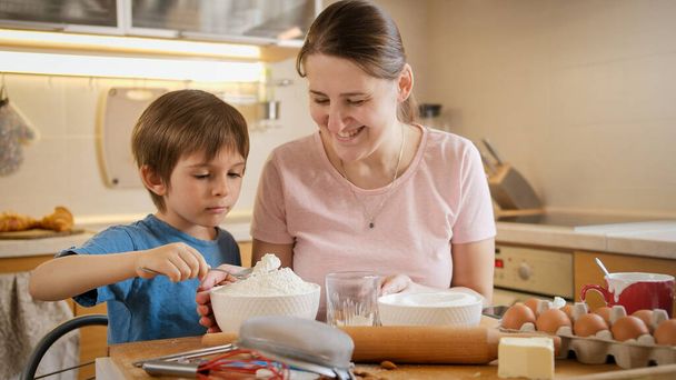 Kleine jongen met jonge moeder die ingrediënten controleert en weegt op digitale weegschalen. Kinderen koken met ouders, kleine chef-kok, familie hebben tijd samen, huishoudelijke keuken. - Foto, afbeelding
