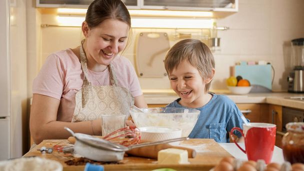 Mutlu gülen çocuk, annesi evde bisküvi pişirirken oynaşıp oynaşıyor. Çocuklar aileleriyle yemek pişirir, küçük aşçı olur, aile birlikte vakit geçirir, ev mutfağı olur.. - Fotoğraf, Görsel