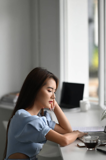 Retrato de freelancer feminino sentado em seu escritório enquanto olha para a tela do laptop. - Foto, Imagem