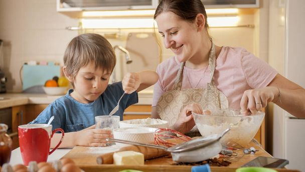 Kleiner Junge hilft Mutter beim Teigbacken für Kekse. Kinder kochen mit Eltern, kleiner Koch, gemeinsame Zeit mit der Familie, häusliche Küche. - Foto, Bild