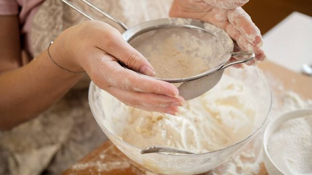 Widok z góry żeńskiej mąki przesiewającej piekarz sitem w dużej szklanej misce do wyrobu ciasta. - Zdjęcie, obraz
