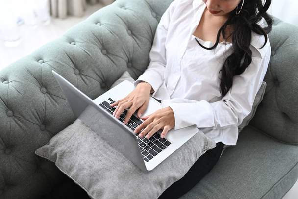 Обрізаний знімок розслабленої дівчини, що використовує ноутбук на дивані у вітальні вдома
. - Фото, зображення