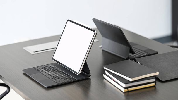 Dunkler, moderner Arbeitsplatz mit leerem Bildschirm-Tablet auf schwarzem Schreibtisch. - Foto, Bild