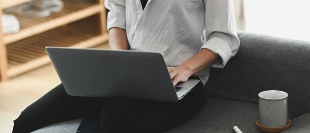 Rajattu laukaus nuori nainen levätä sohvalla kotona selailu langaton Internet kannettavalla tietokoneella. - Valokuva, kuva