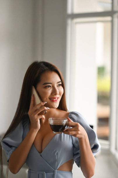 Portrait of attractive businesswoman talking on mobile phone and drinking coffee in the morning. - Photo, Image