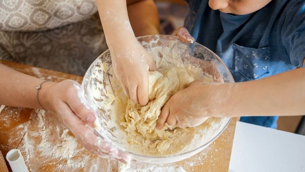 Closeup of little boy kneading dough in glass bowl on kitchen - Photo, image