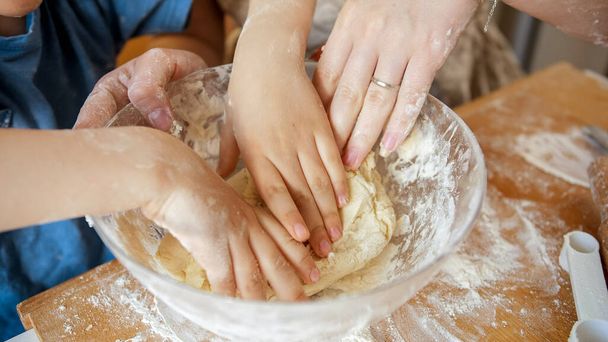 Closeup of mothers and childs hands kneading dough ingredients in glass bowl while making biscuits. Children cooking with parents, little chef, family having time together, domestic kitchen. - Photo, Image