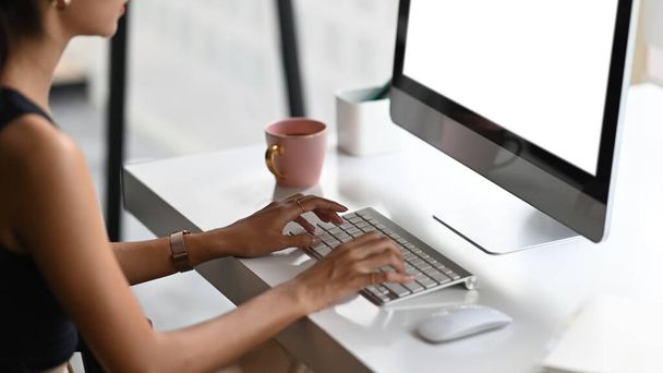 Cropped shot of professional designer typing on blank screen computer in minimal workspace on white table. - Photo, Image
