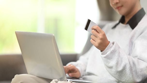 Recorte de una joven con tarjeta de crédito y tableta de ordenador en el sofá en casa. - Foto, Imagen