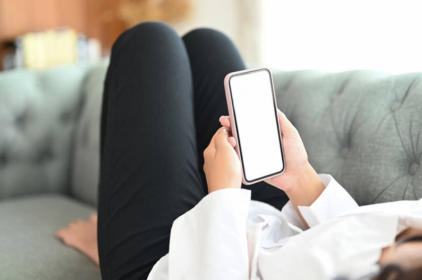 Cropped shot of female freelancer relaxing on couch and using smart phone with blank screen at home. - Fotografie, Obrázek