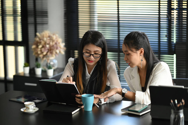 Jóvenes empresarias asiáticas trabajando juntas en el cargo mientras están sentadas leyendo un informe o papeleo. - Foto, imagen