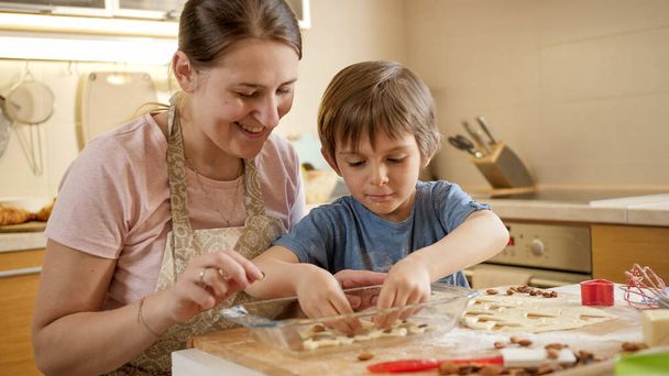 母を持つ幸せな笑顔の男の子はビスケットを作り、ベーキングフォームに入れます。両親、小さなシェフ、家族と一緒に時間を過ごす子供たち、家庭用キッチン. - 写真・画像