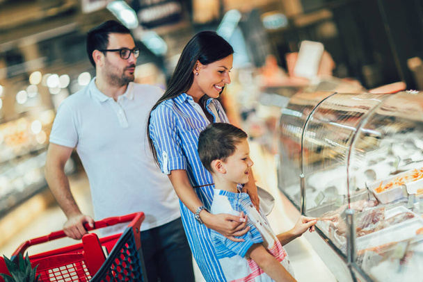 Szczęśliwa rodzina z dzieckiem i wózkiem zakupowym kupując żywność w sklepie spożywczym lub supermarkecie - Zdjęcie, obraz