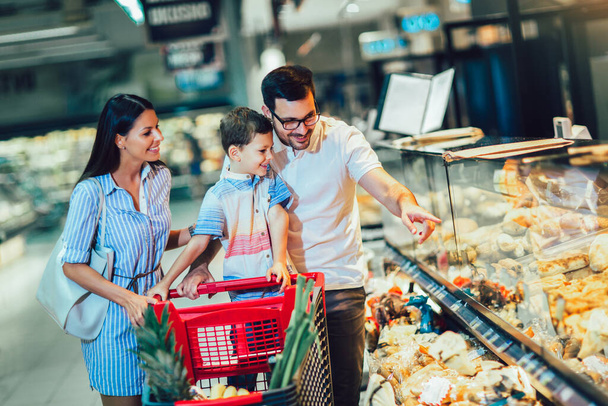 Boldog család gyermekkel és bevásárlókosárral élelmiszert vásárol élelmiszerboltban vagy szupermarketben - Fotó, kép