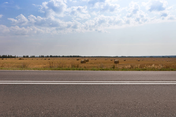 Highway along a field with rolls of hay on a sunny autumn day. - Φωτογραφία, εικόνα