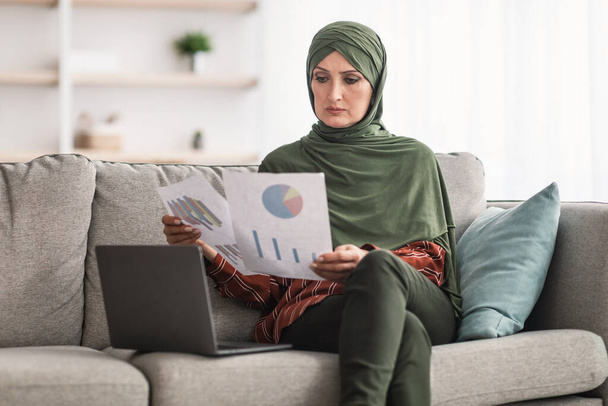 Мусульманська бізнес-леді за допомогою ноутбука Дивлячись Статистичні діаграми Робота в приміщенні
 - Фото, зображення
