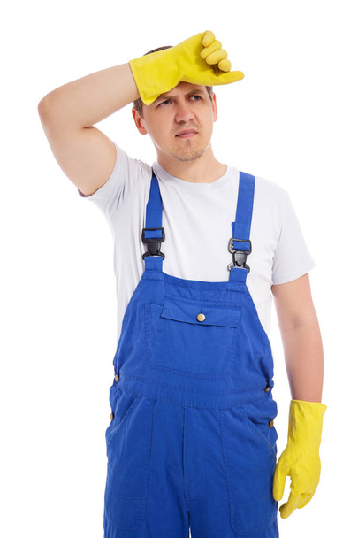 портрет уставшего мужчины-уборщика в синей униформе и желтых перчатках на белом фоне - Фото, изображение