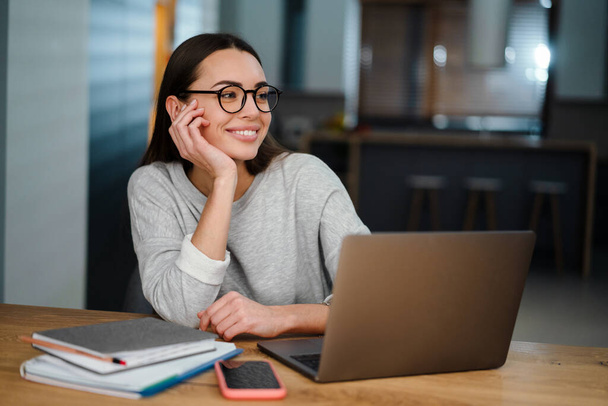Happy young woman in eyeglasses smiling while working with laptop at home - Φωτογραφία, εικόνα