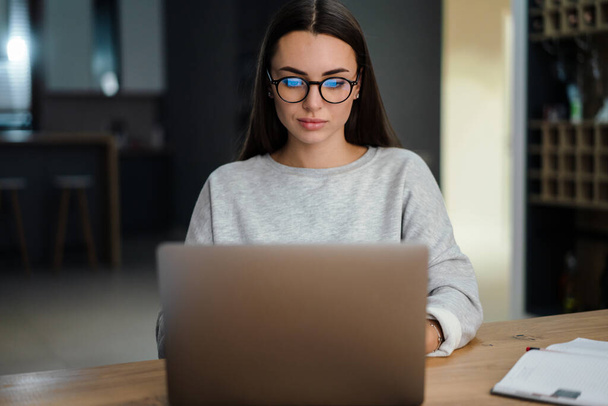 Brunette concentré jeune femme dans les lunettes de travail avec ordinateur portable à la maison - Photo, image
