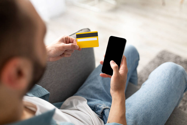 Online-Bestellung. Unbekannter junger Mann mit Kreditkarte und Smartphone im Internet unterwegs, Attrappe - Foto, Bild