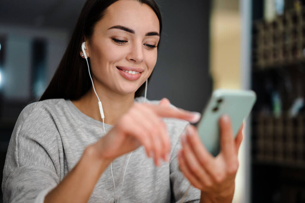 Happy young woman listening music with earphones and mobile phone while sitting at home - Foto, Imagen