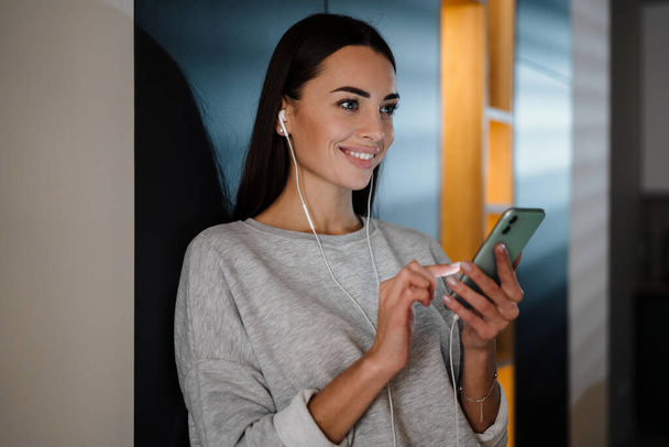 Smiling young woman listening music with earphones and mobile phone at home - Фото, зображення
