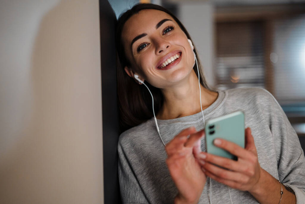 Smiling young woman listening music with earphones and mobile phone at home - Photo, Image